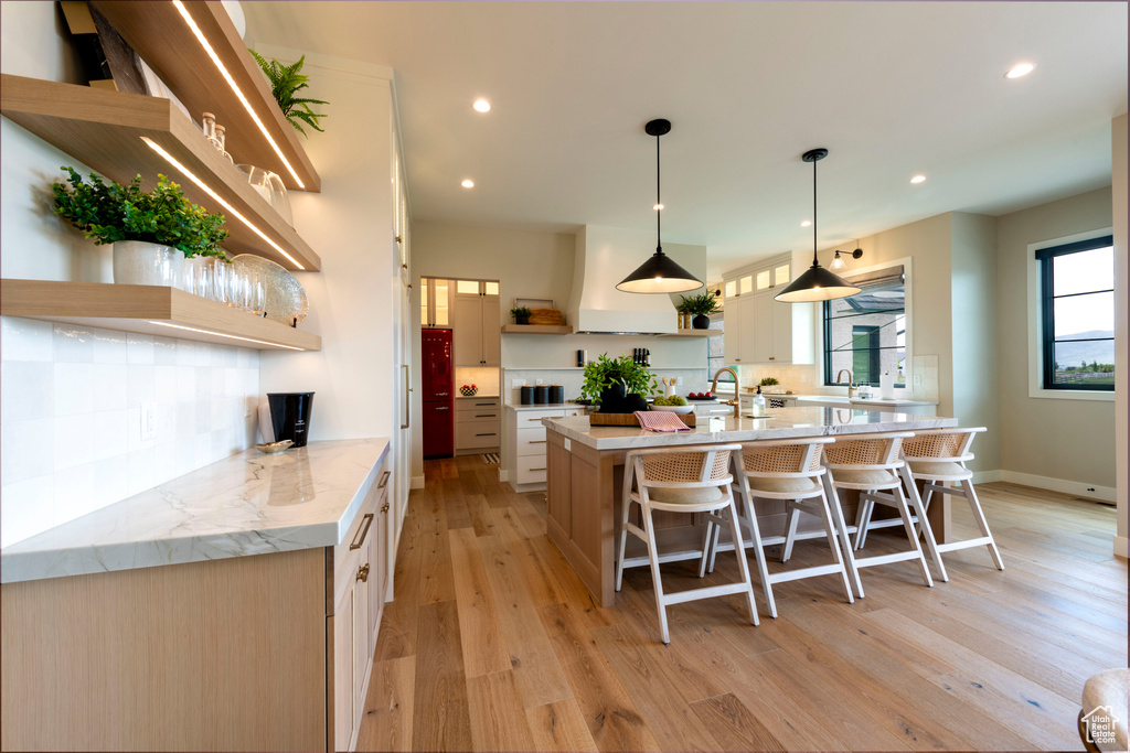 Kitchen featuring open shelves, a spacious island, light wood-type flooring, a breakfast bar area, and recessed lighting