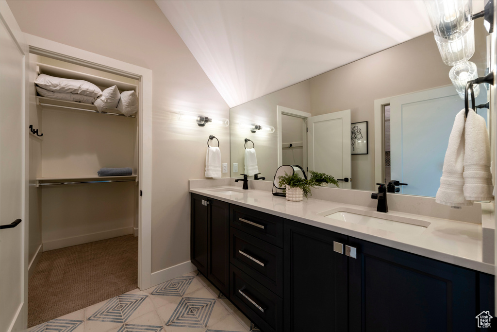 Bathroom featuring double vanity, lofted ceiling, and a spacious closet