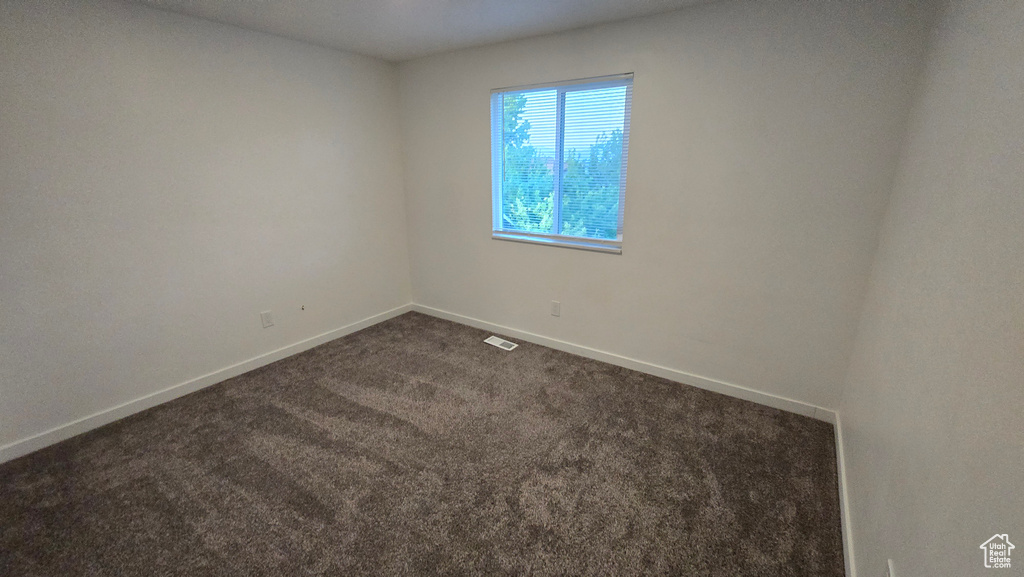 Unfurnished room featuring dark carpet and baseboards