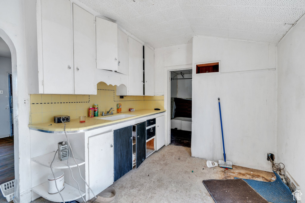 Kitchen with vaulted ceiling, white cabinets, arched walkways, and light countertops