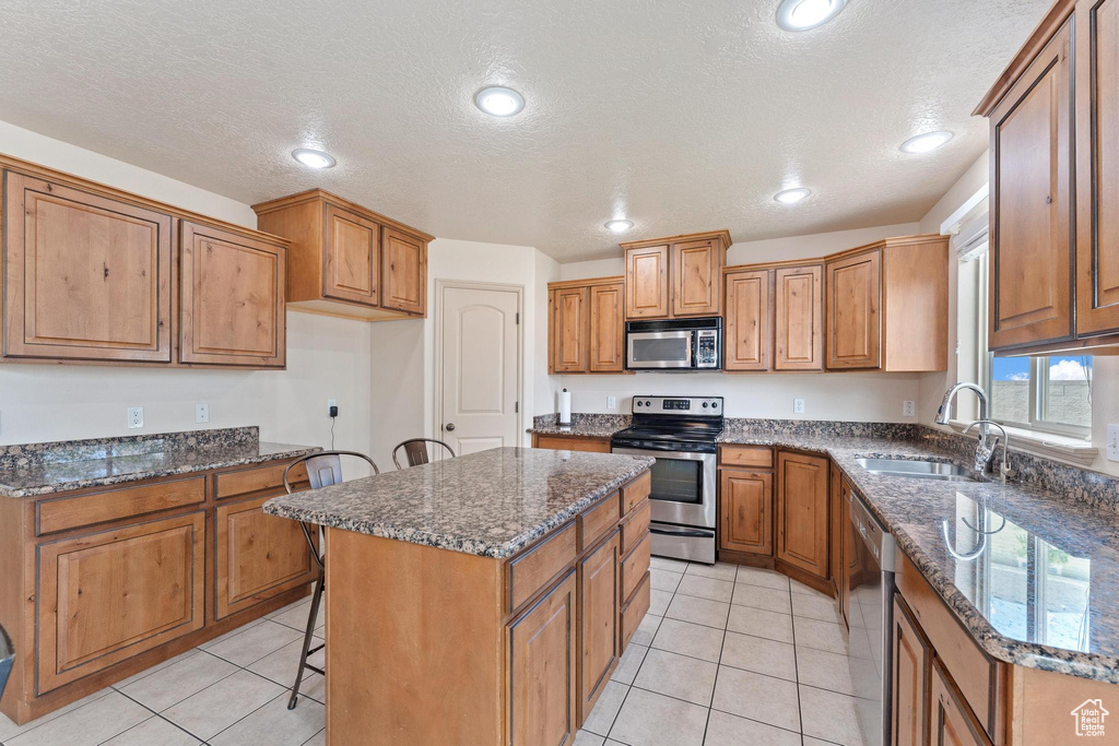 Kitchen featuring appliances with stainless steel finishes, brown cabinets, a center island, dark stone counters, and a textured ceiling