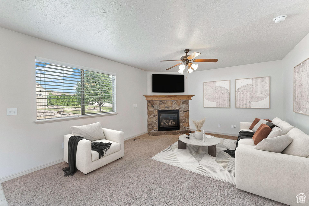Living area featuring a fireplace, a ceiling fan, carpet flooring, and a textured ceiling