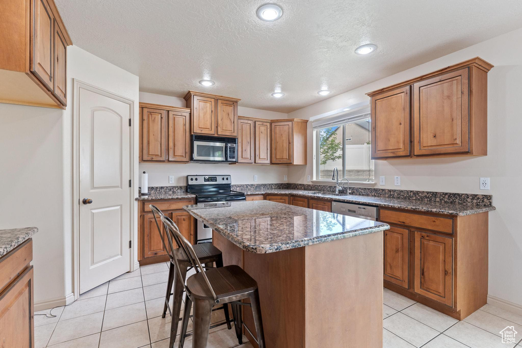 Kitchen with appliances with stainless steel finishes, brown cabinetry, a kitchen island, a breakfast bar, and light tile patterned floors