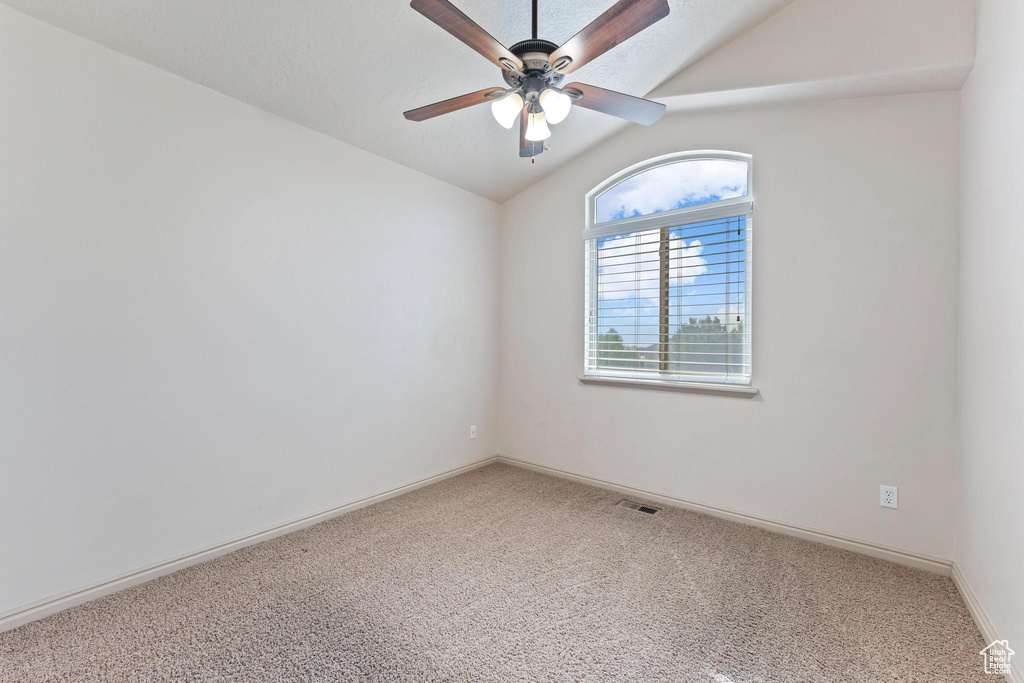 Carpeted spare room featuring lofted ceiling and a ceiling fan