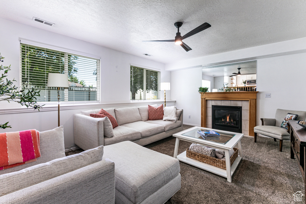 Carpeted living room with a ceiling fan, a fireplace, and a textured ceiling