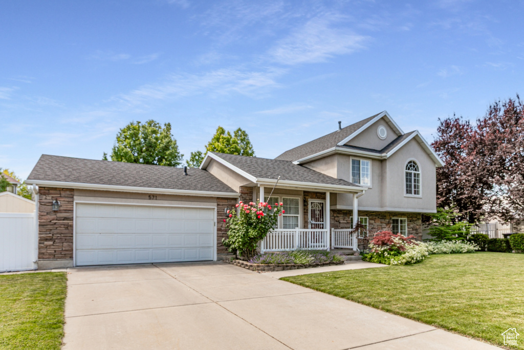 Split level home featuring stone siding, a porch, a front yard, concrete driveway, and an attached garage