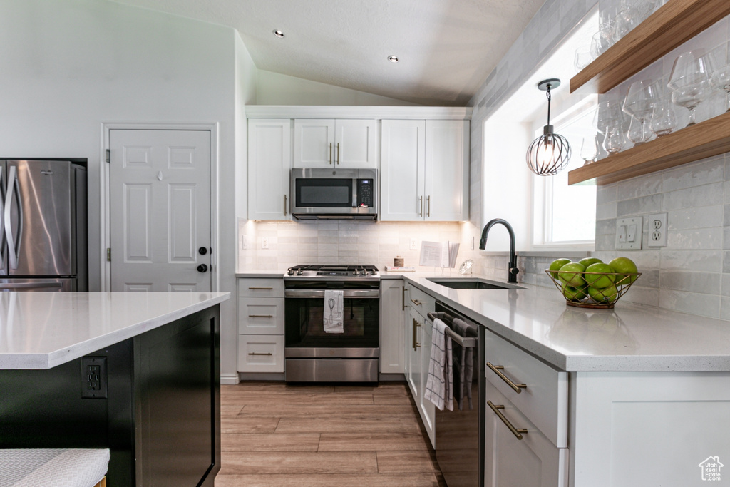 Kitchen with stainless steel appliances, white cabinets, lofted ceiling, light wood-style floors, and open shelves