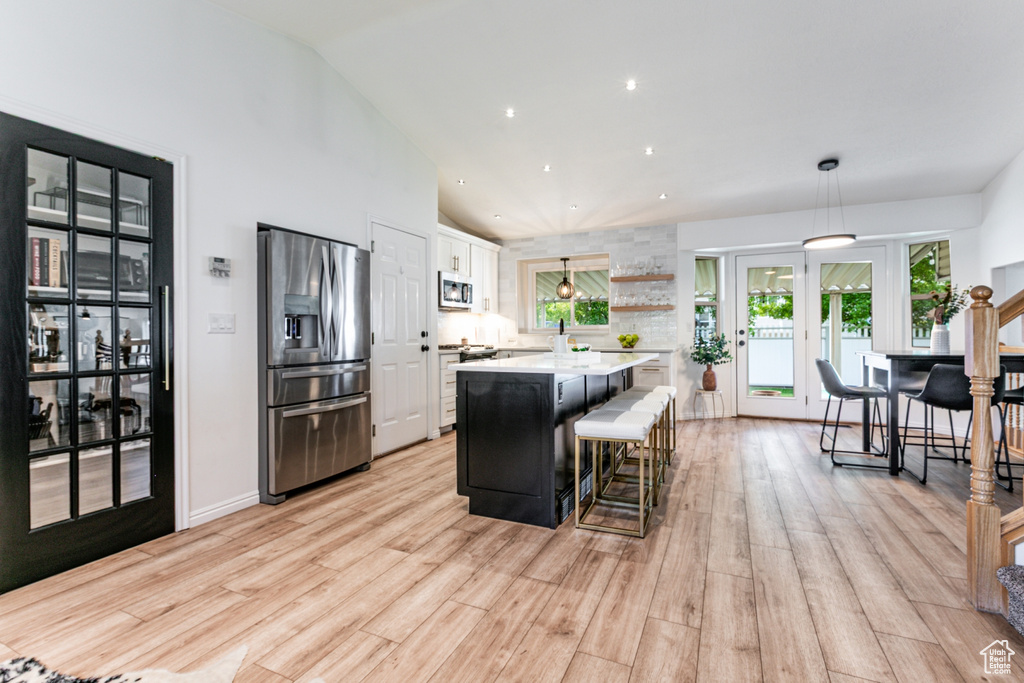 Kitchen with stainless steel appliances, white cabinets, light countertops, a center island, and light wood-style flooring