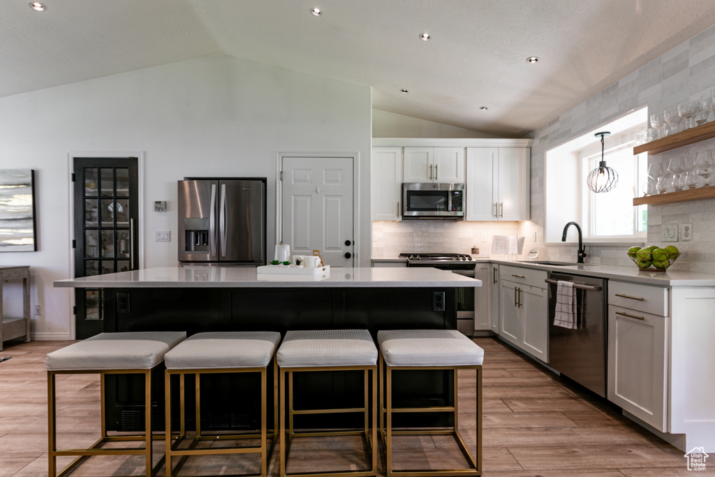 Kitchen with appliances with stainless steel finishes, vaulted ceiling, a kitchen breakfast bar, a kitchen island, and light countertops