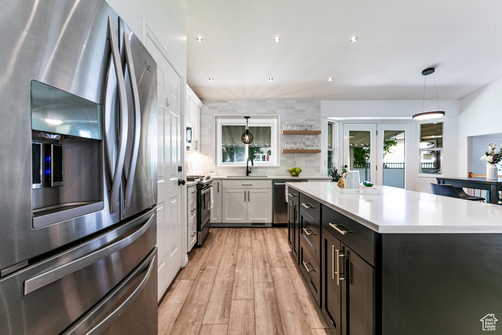 Kitchen with stainless steel appliances, white cabinets, light countertops, light wood-type flooring, and hanging light fixtures