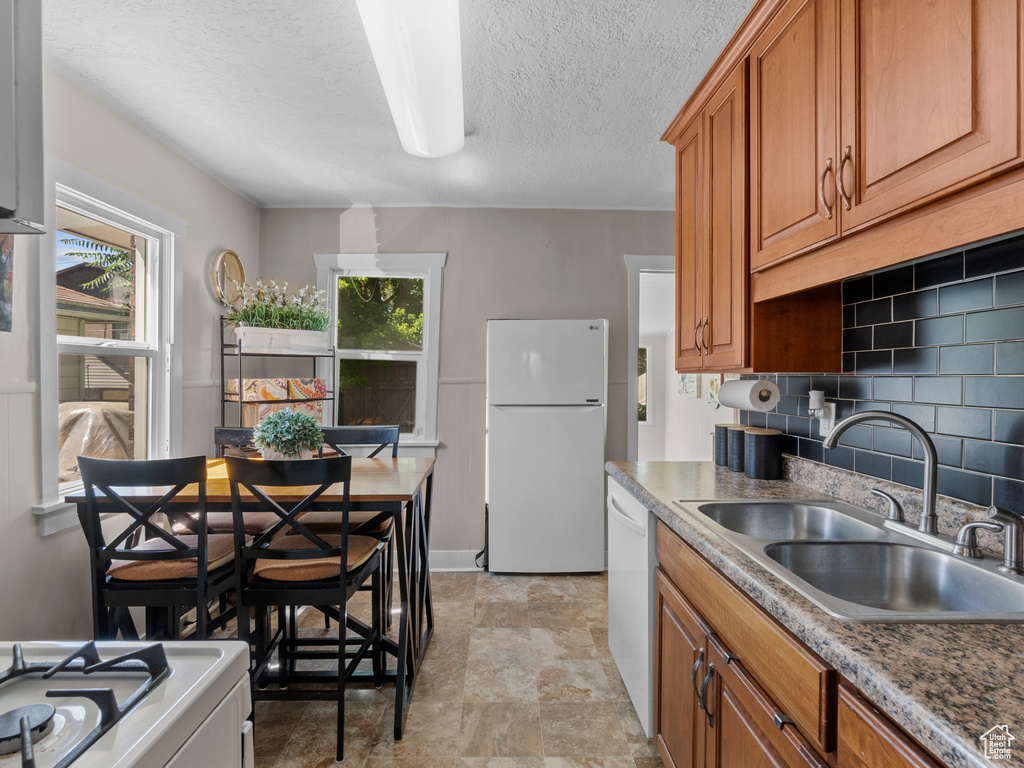 Kitchen with white appliances, brown cabinets, a textured ceiling, stone finish floors, and tasteful backsplash