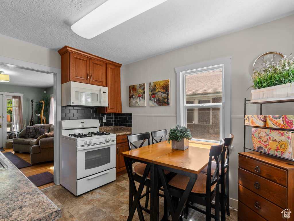 Kitchen with white appliances, brown cabinetry, backsplash, and a textured ceiling