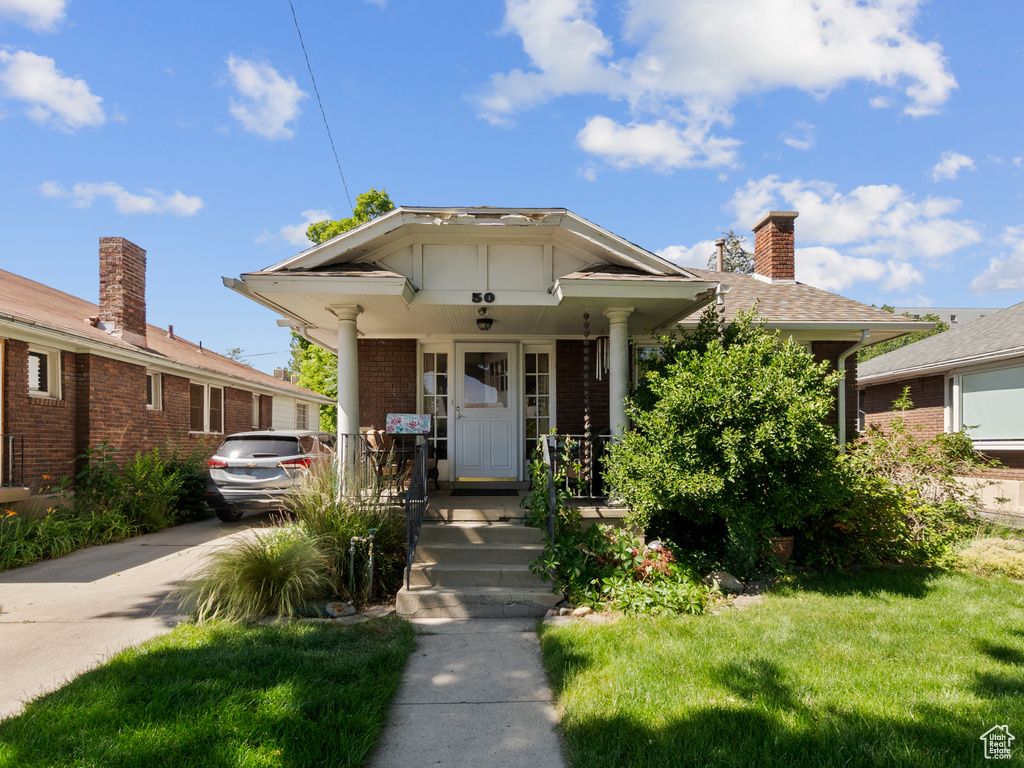View of front of house with covered porch, brick siding, a chimney, concrete driveway, and a front lawn