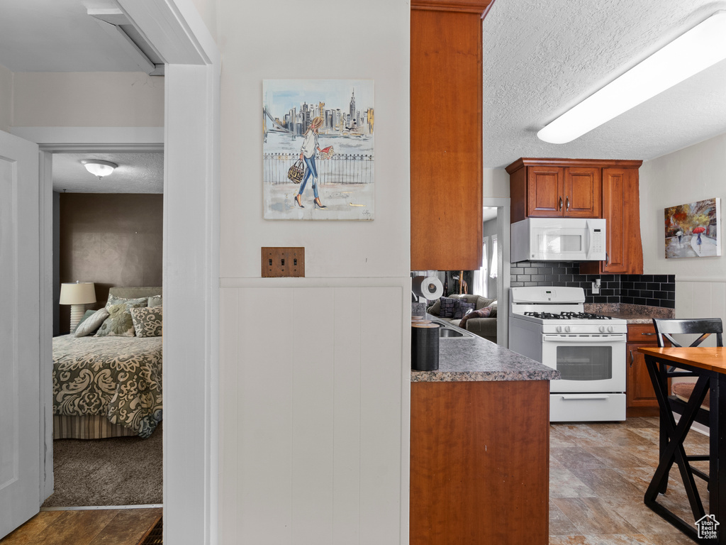 Kitchen featuring white appliances, decorative backsplash, brown cabinetry, and a textured ceiling