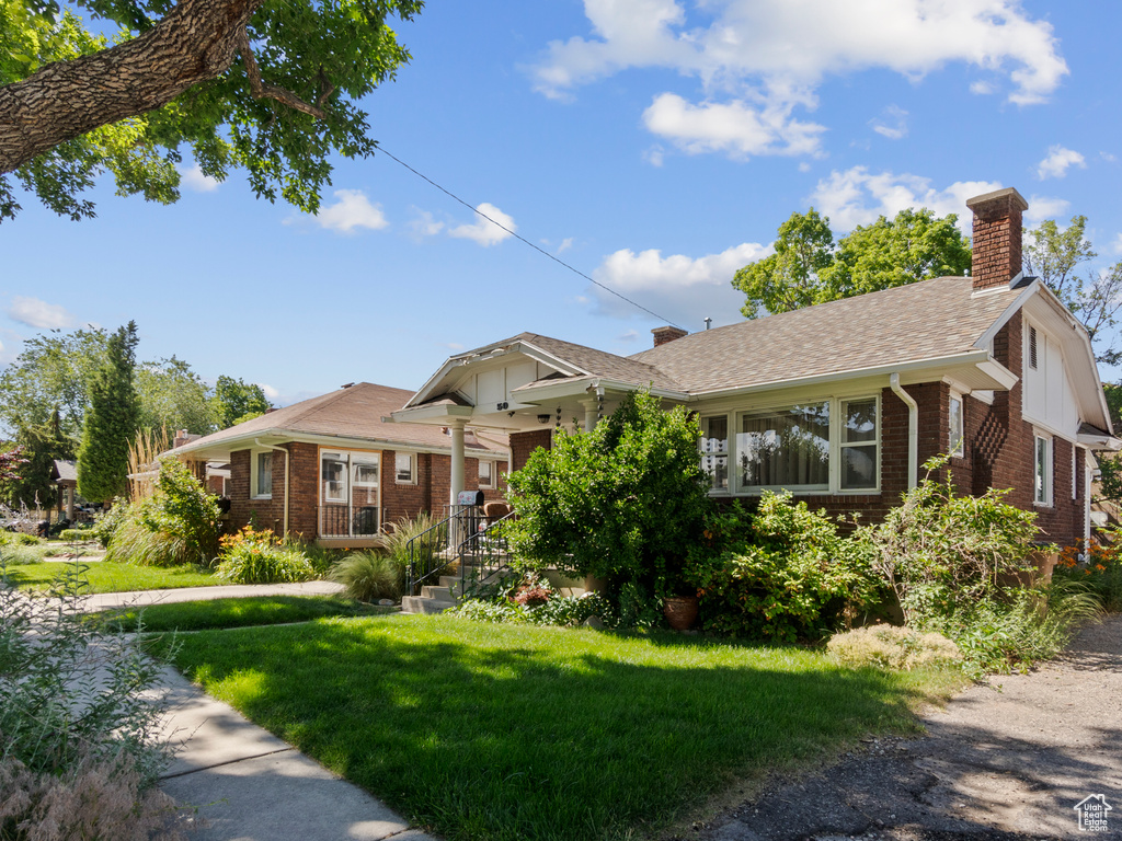Ranch-style home featuring brick siding, a chimney, a front lawn, and a shingled roof