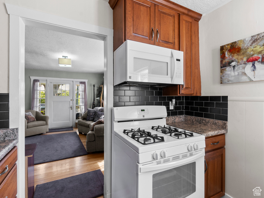 Kitchen with white appliances, brown cabinetry, wood finished floors, open floor plan, and a textured ceiling