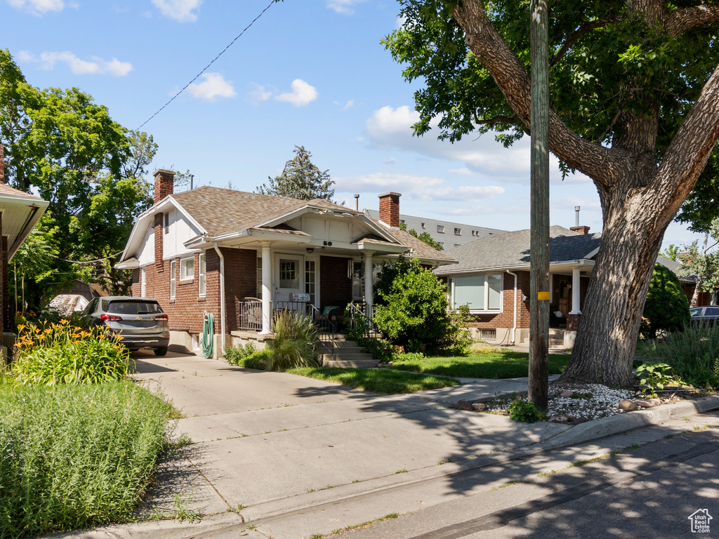 Bungalow-style home with brick siding, concrete driveway, covered porch, and a chimney
