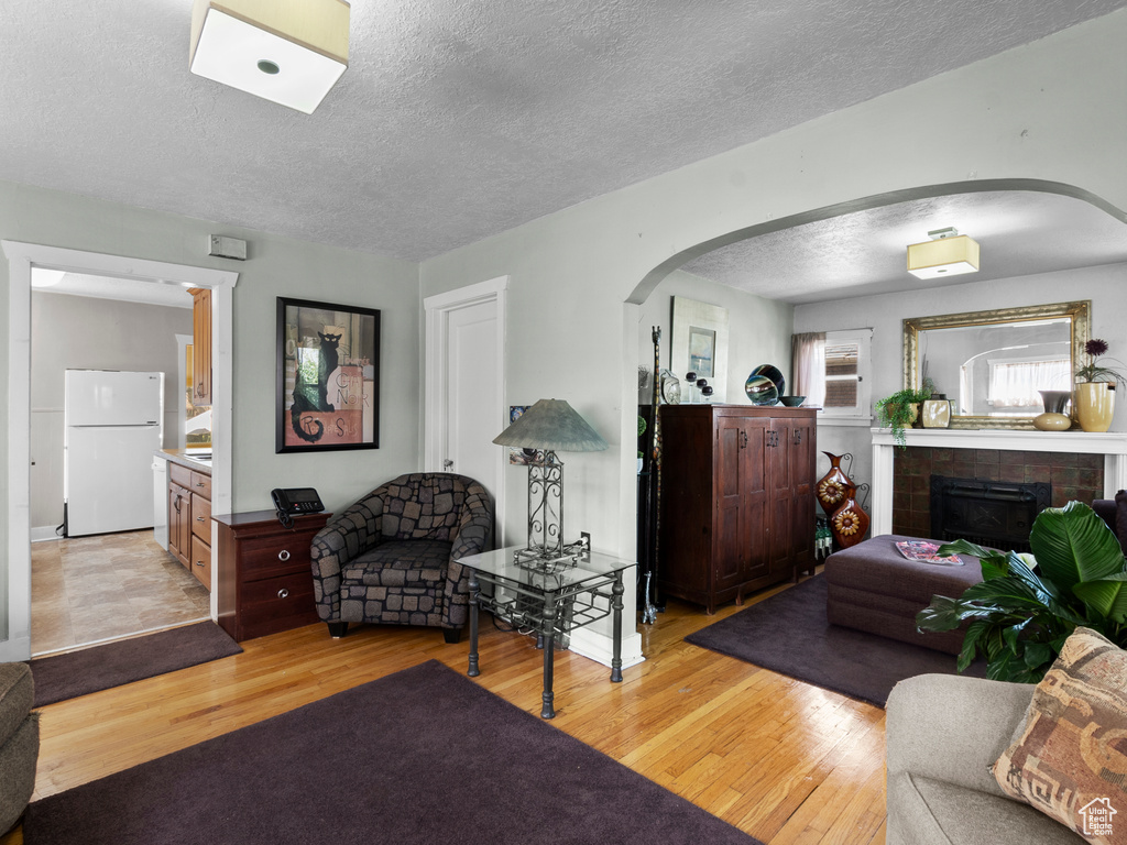 Living area featuring arched walkways, light wood finished floors, a textured ceiling, and a fireplace