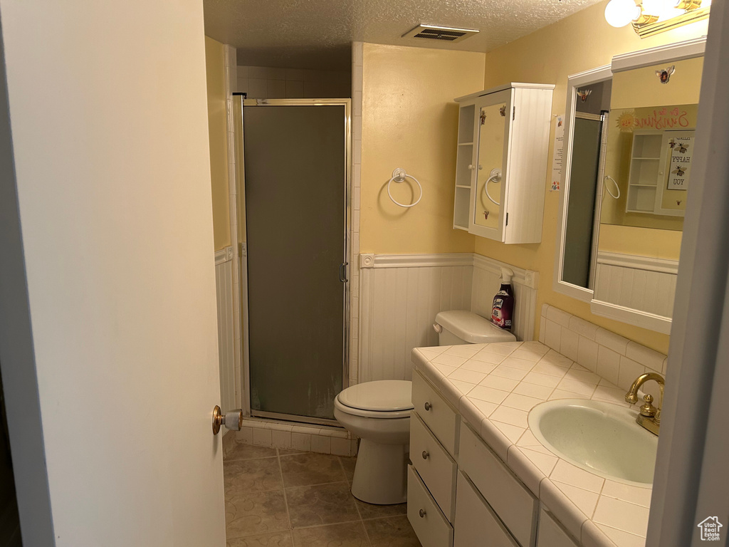 Full bathroom featuring toilet, a wainscoted wall, vanity, a stall shower, and a textured ceiling
