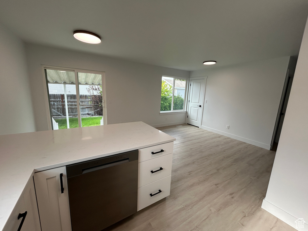 Kitchen with stainless steel dishwasher, light wood-style floors, white cabinets, and light stone countertops