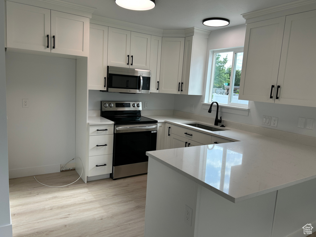 Kitchen featuring stainless steel appliances, a peninsula, white cabinets, light wood-style flooring, and light stone counters