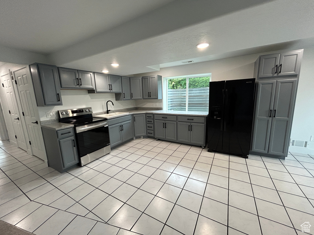 Kitchen with black fridge, stainless steel electric stove, gray cabinetry, light countertops, and light tile patterned flooring