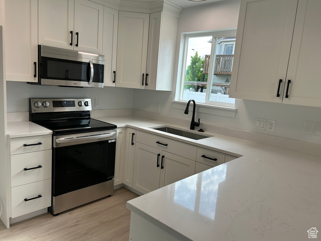 Kitchen featuring stainless steel appliances, white cabinets, light wood-style floors, and light stone counters