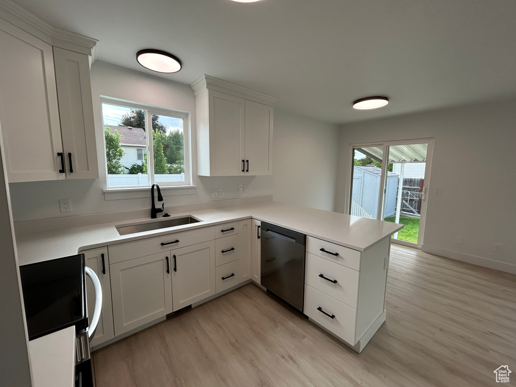Kitchen with dishwasher, light wood-style floors, a peninsula, and healthy amount of natural light