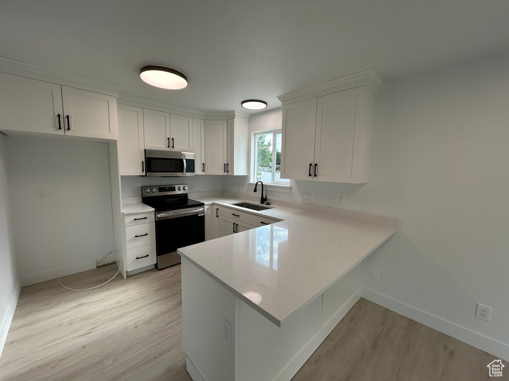 Kitchen with stainless steel appliances, light wood-type flooring, a peninsula, and white cabinetry