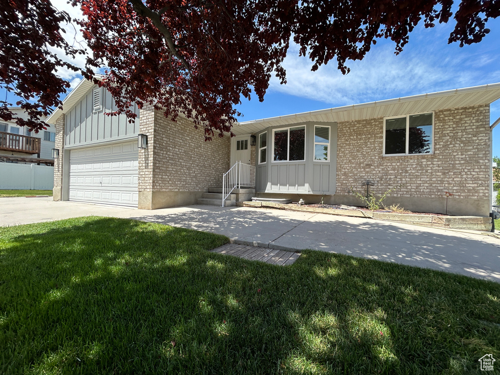 Ranch-style home with brick siding, board and batten siding, a front yard, and a garage