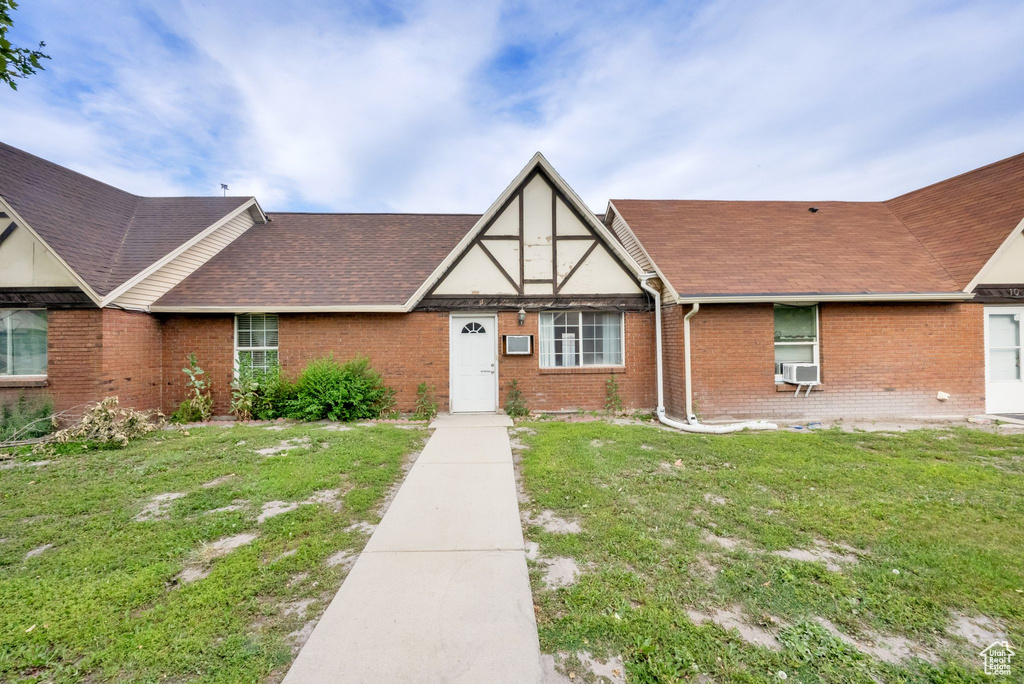 View of front of house with brick siding, roof with shingles, a front yard, and cooling unit