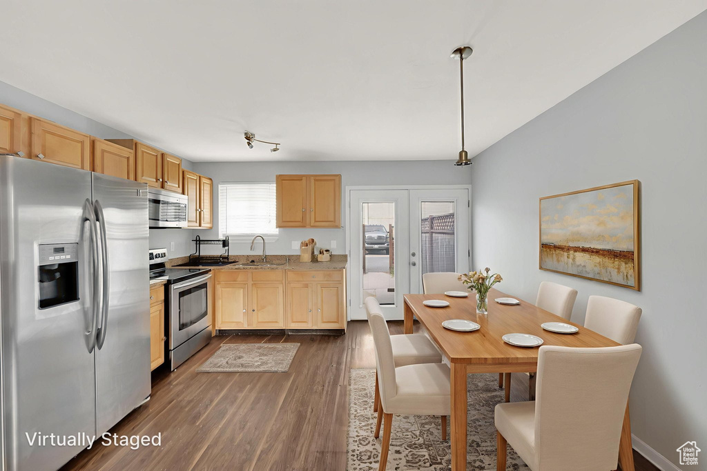 Kitchen featuring stainless steel appliances, light brown cabinetry, dark wood-type flooring, light countertops, and hanging light fixtures