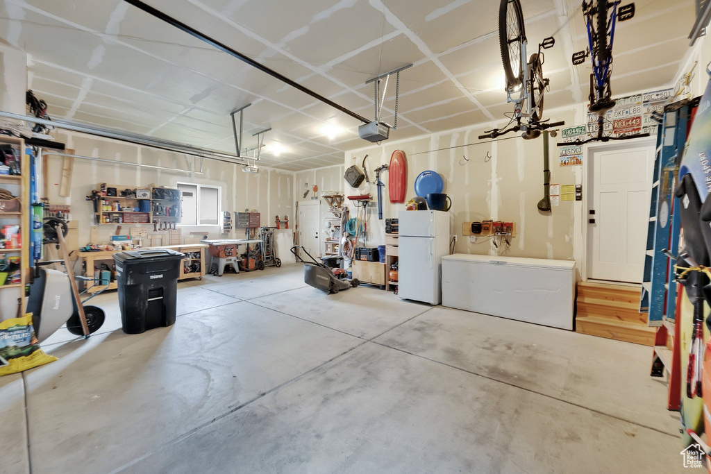 Garage with freestanding refrigerator, a garage door opener, and a workshop area