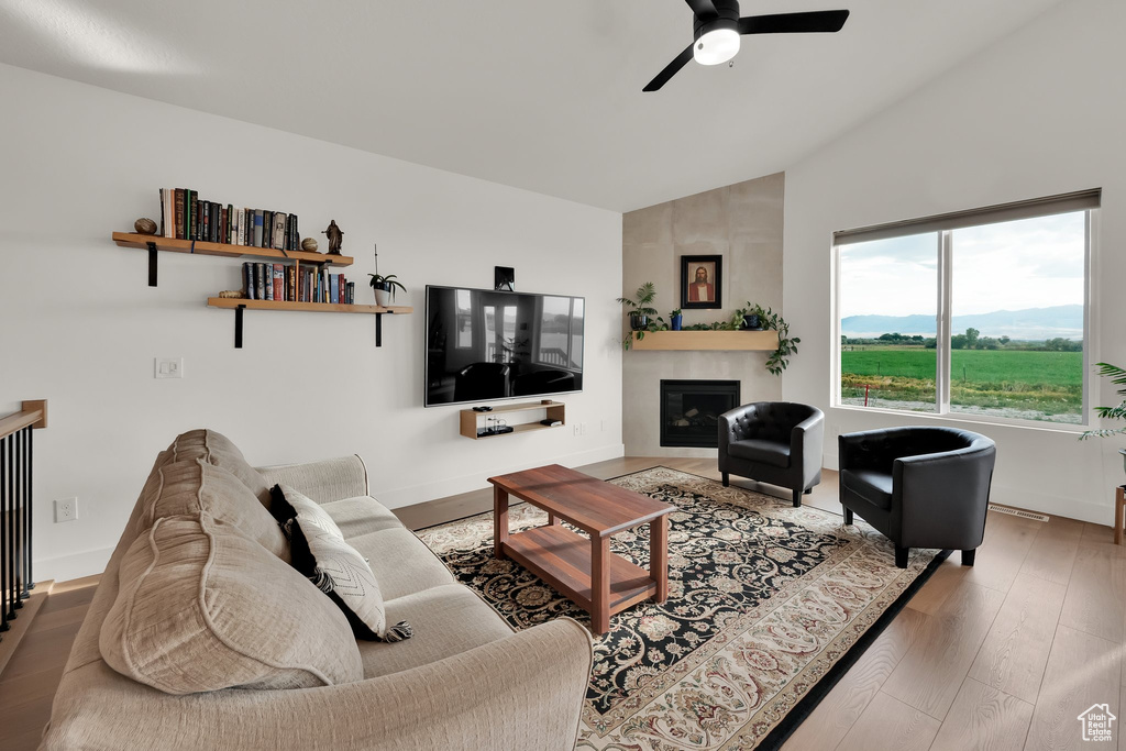 Living room featuring a ceiling fan, wood finished floors, a large fireplace, and high vaulted ceiling