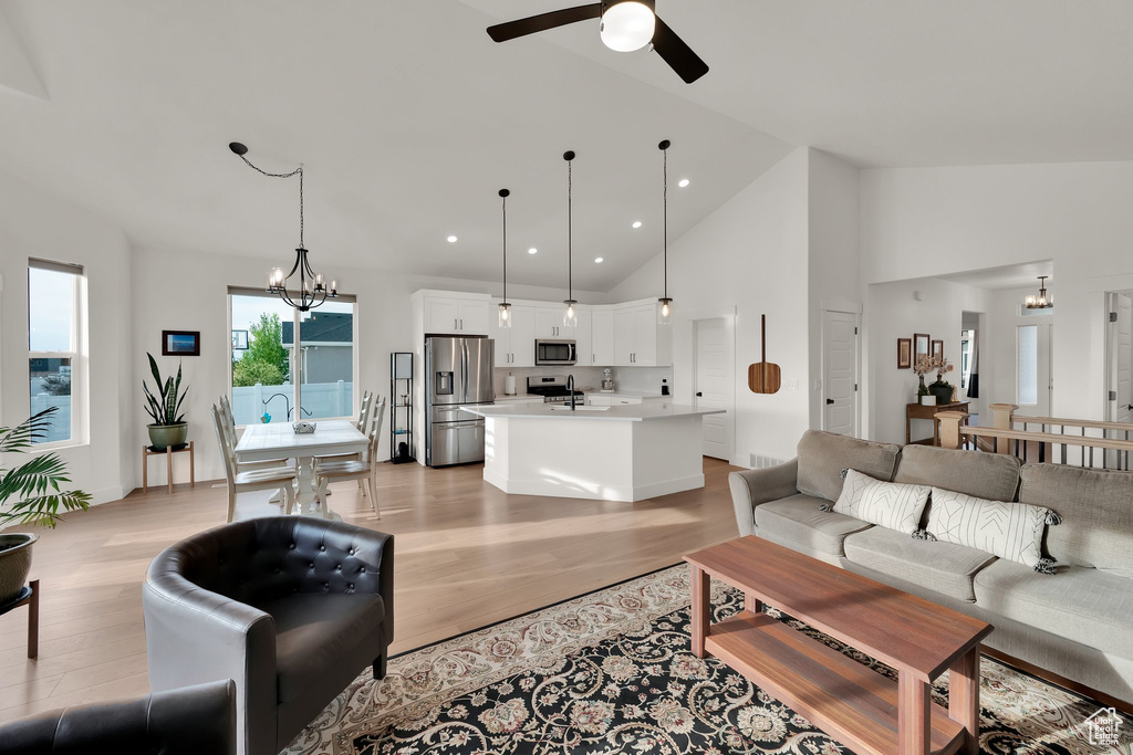 Living area with light wood-style floors, a chandelier, ceiling fan, recessed lighting, and high vaulted ceiling