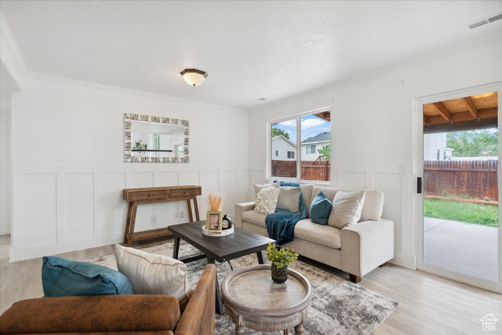 Living room featuring light wood-style flooring, a decorative wall, a wainscoted wall, and ornamental molding