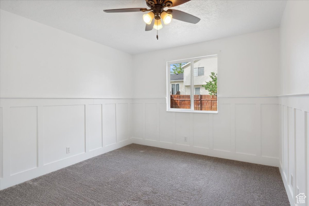 Unfurnished room with a decorative wall, carpet, ceiling fan, and wainscoting