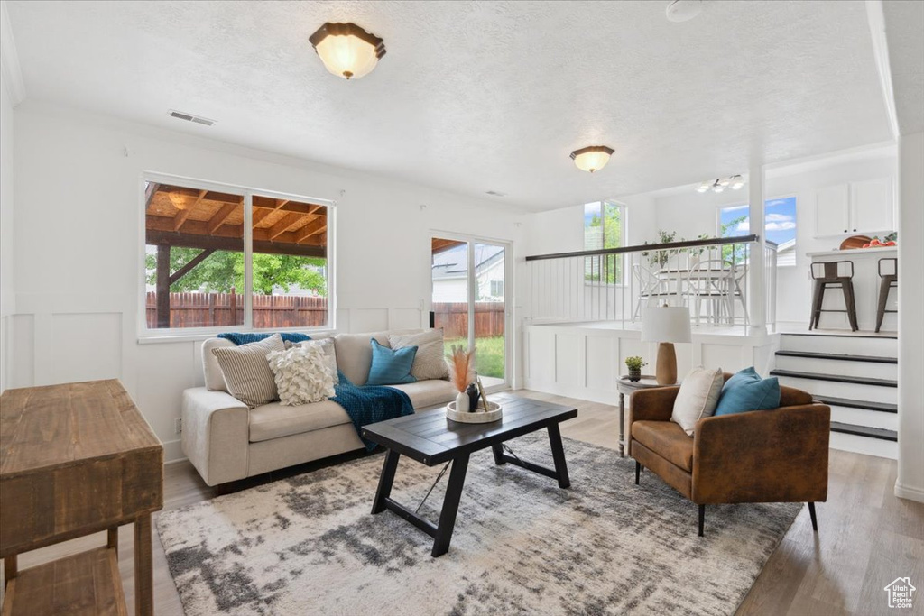 Living room featuring a textured ceiling, a decorative wall, wood finished floors, and a wainscoted wall