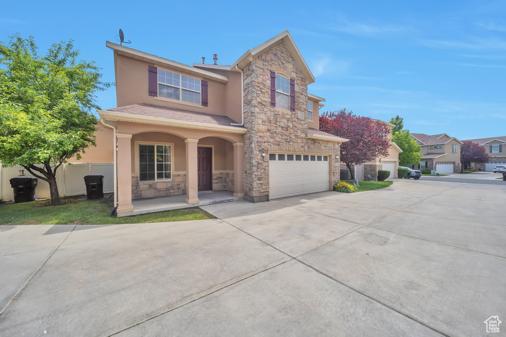 Traditional home with a porch, stone siding, stucco siding, an attached garage, and concrete driveway