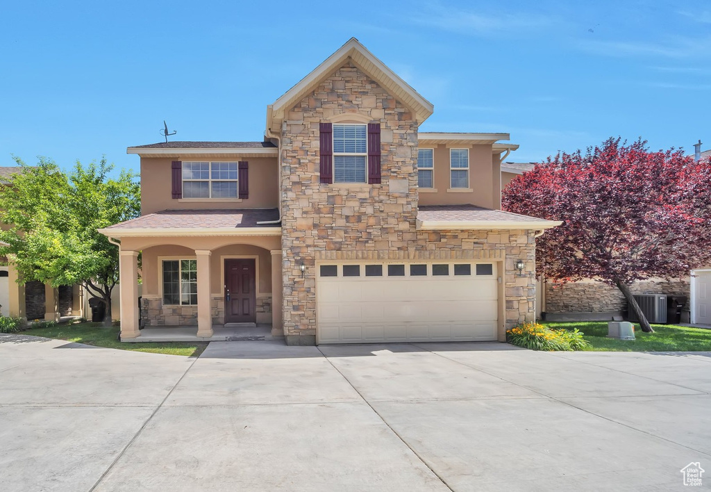 Traditional home with stone siding, stucco siding, driveway, an attached garage, and a porch