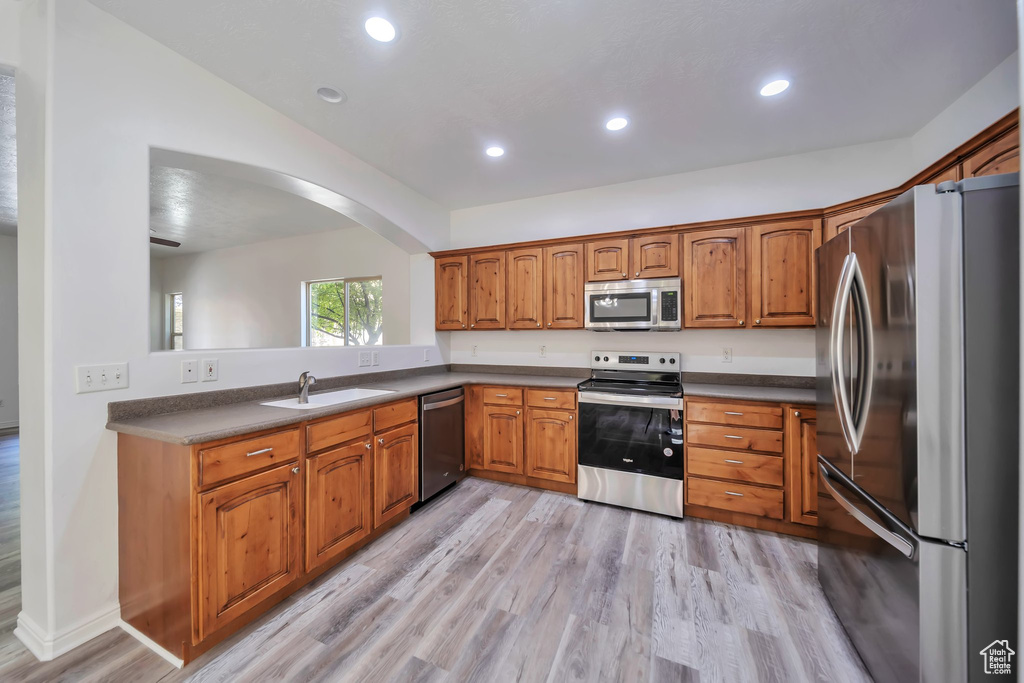 Kitchen with appliances with stainless steel finishes, brown cabinetry, light wood-style flooring, arched walkways, and recessed lighting