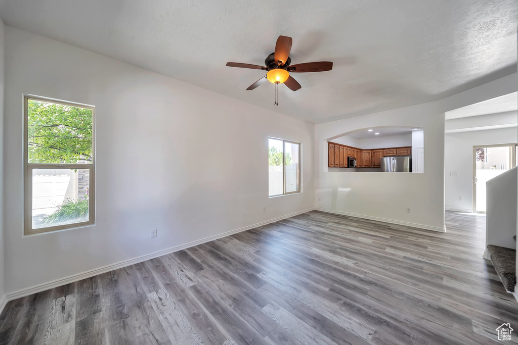Unfurnished living room with healthy amount of natural light, ceiling fan, and wood finished floors