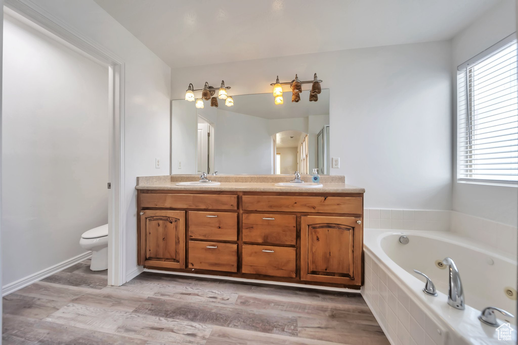 Bathroom with double vanity, a jetted tub, healthy amount of natural light, and wood finished floors