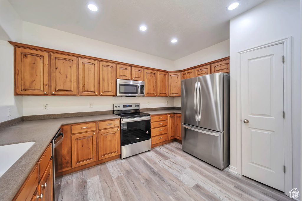Kitchen with appliances with stainless steel finishes, brown cabinets, light wood-style flooring, and recessed lighting