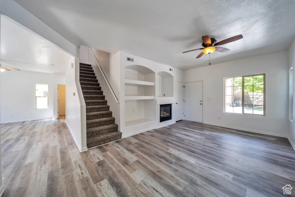 Unfurnished living room with a ceiling fan, built in features, and wood finished floors