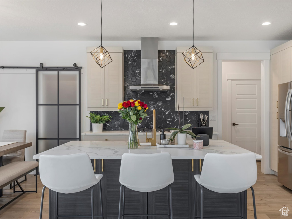 Kitchen featuring wall chimney range hood, tasteful backsplash, stainless steel fridge, a kitchen breakfast bar, and light wood finished floors