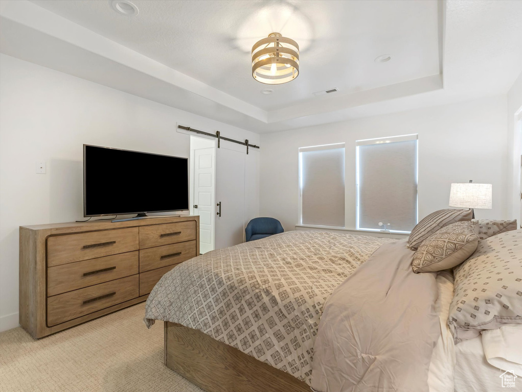 Bedroom featuring a barn door, a raised ceiling, and light carpet