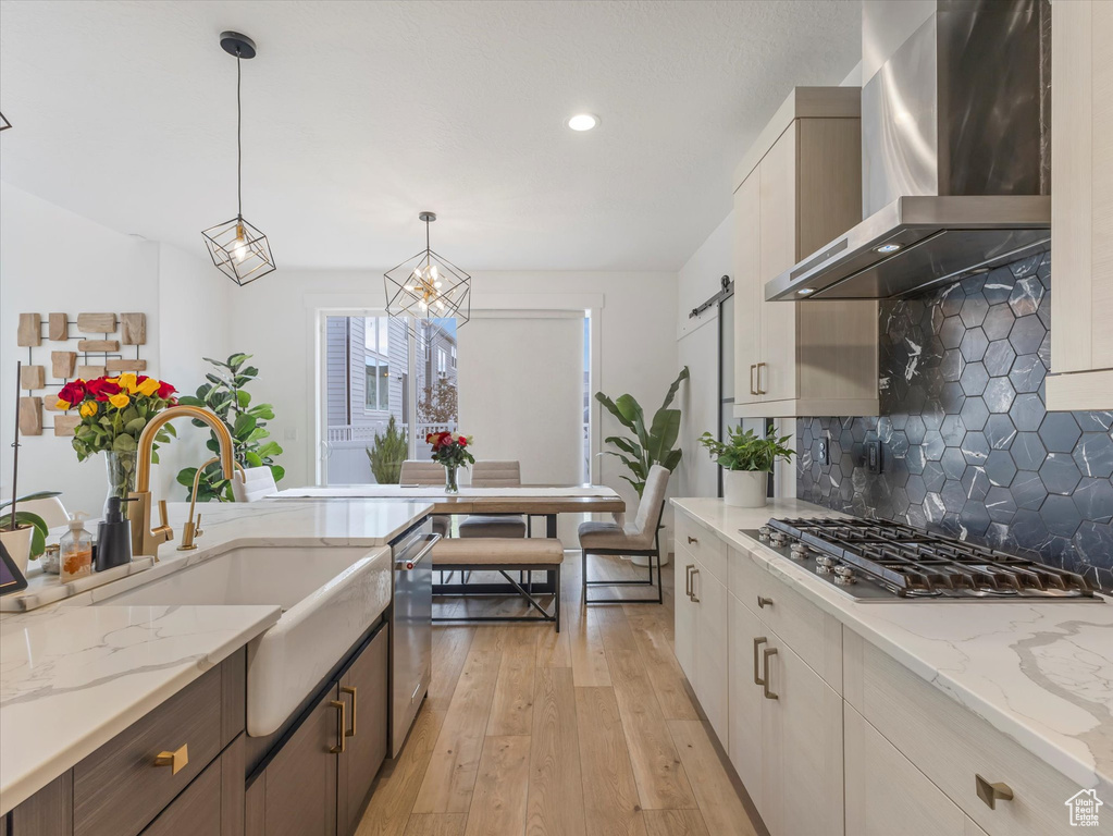 Kitchen featuring wall chimney exhaust hood, appliances with stainless steel finishes, light wood-style flooring, tasteful backsplash, and a barn door