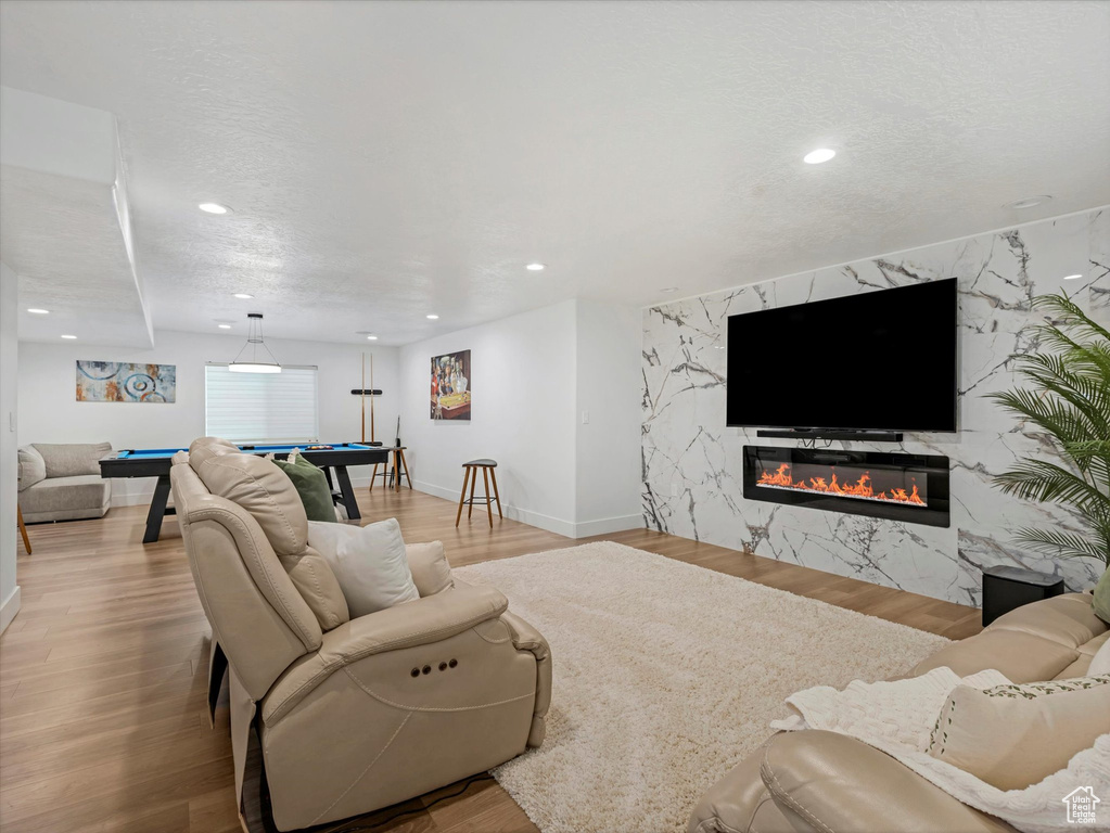 Living area featuring billiards table, recessed lighting, a premium fireplace, wood finished floors, and an accent wall