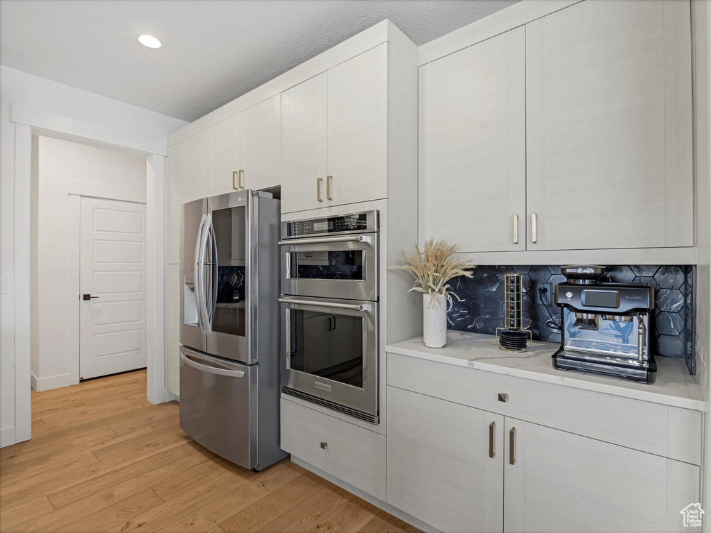 Kitchen featuring appliances with stainless steel finishes, light wood-type flooring, light countertops, white cabinetry, and recessed lighting